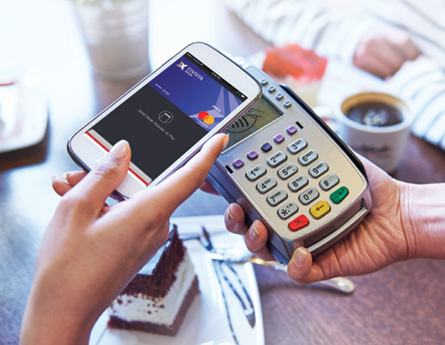 woman's hand holding phone over pay devices at cafe.