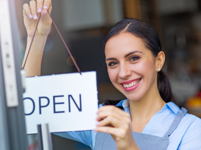 Happy woman changes sign on the door of a business to "open" 