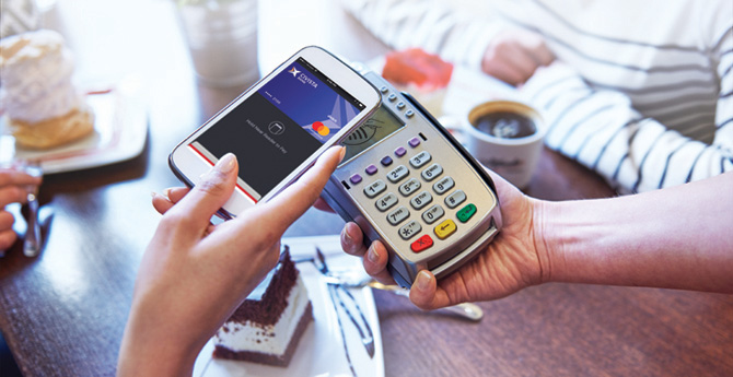 woman's hand holding phone over pay devices at cafe.