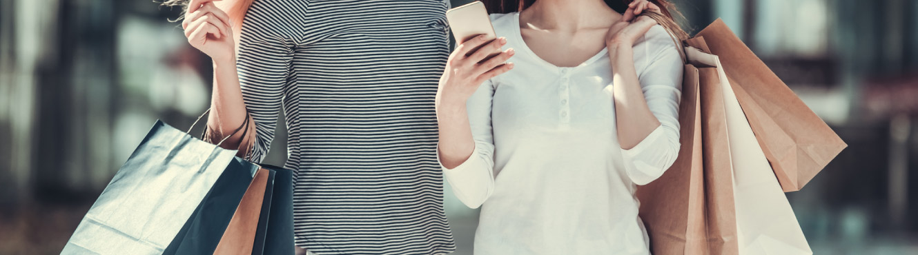 Two women carrying shopping bags and glancing at mobile phone