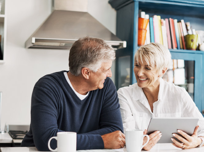 Man and woman sit happily at the kitchen island in discussion while holding a tablet