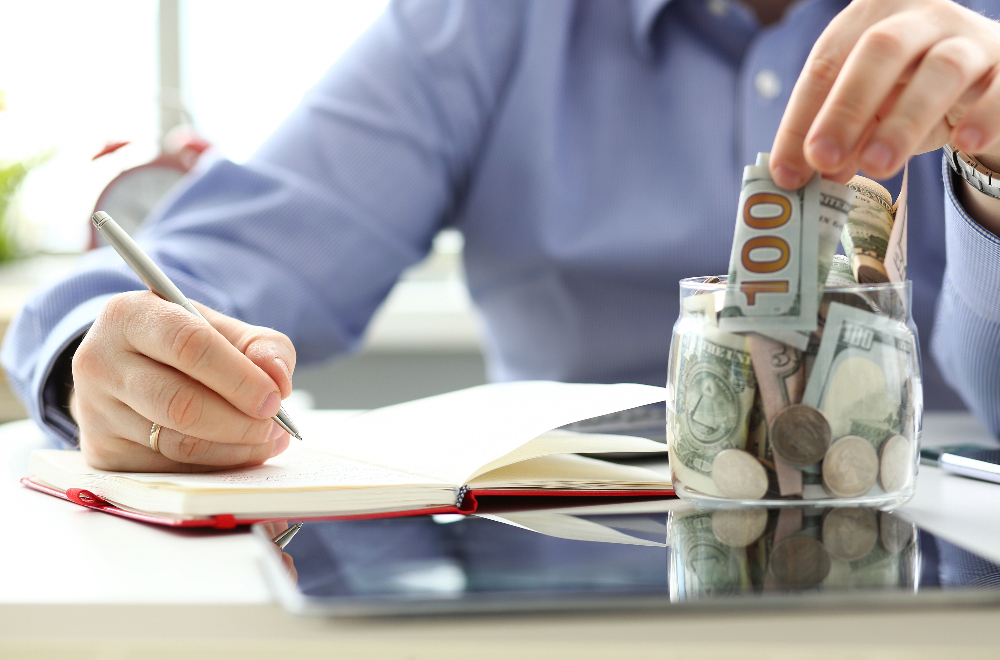 A hand reviewing his savings and putting money into a jar.