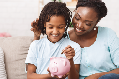 Mother helping daughter save money in piggy bank