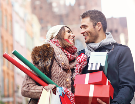 Couple walking and smiling while carrying their holiday shopping.