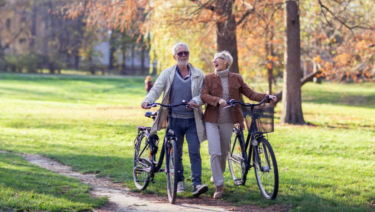 Older couple walking their bikes and laughing.