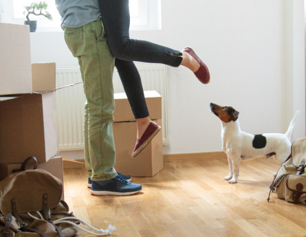Man joyfully holding woman up with moving boxes and pet dog around them