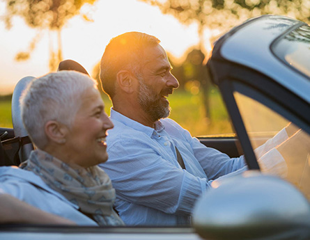 Retired couple driving in a convertible car.