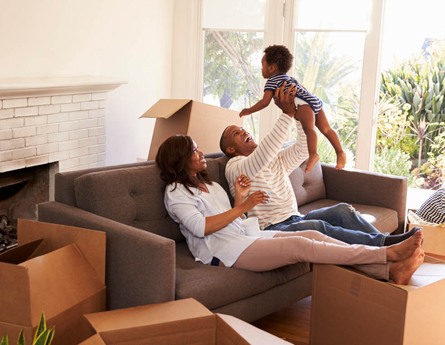 Family sitting on couch celebrating new home holding baby boy in air