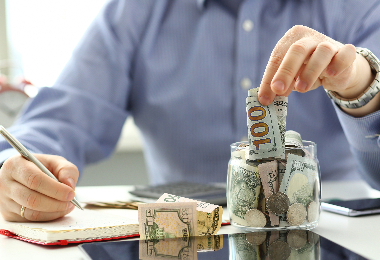 A hand reviewing his savings and putting money into a jar.