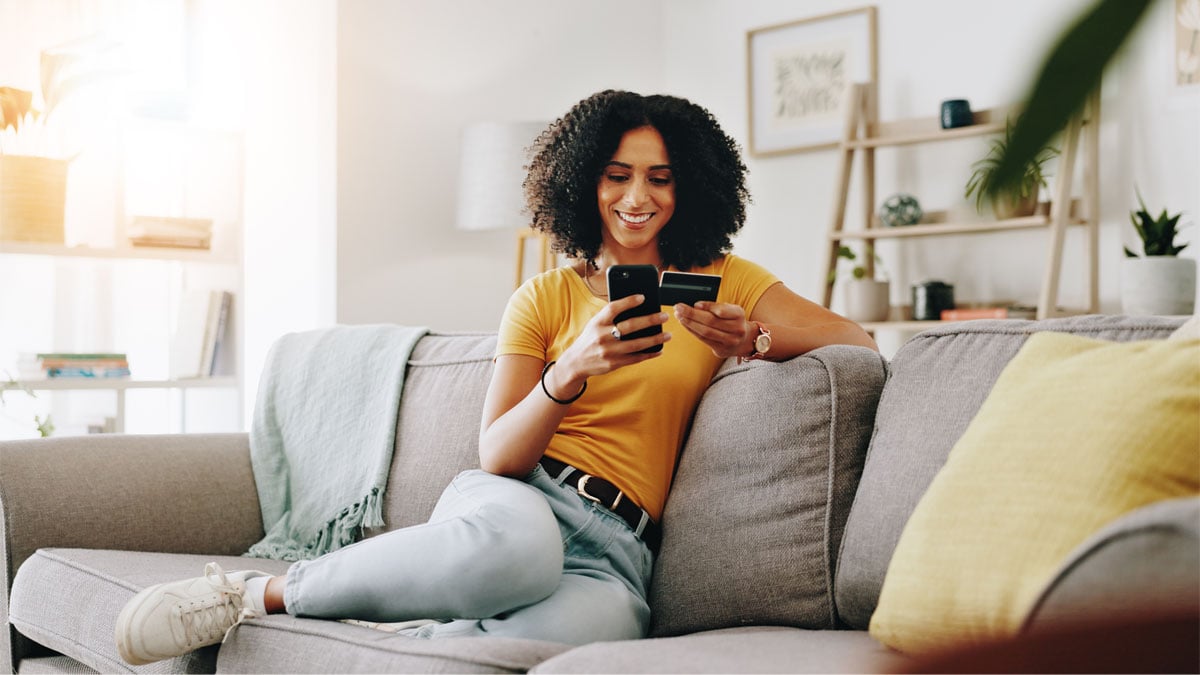 Debit card, happy and woman on sofa with phone for online shopping, web store sale and purchase.