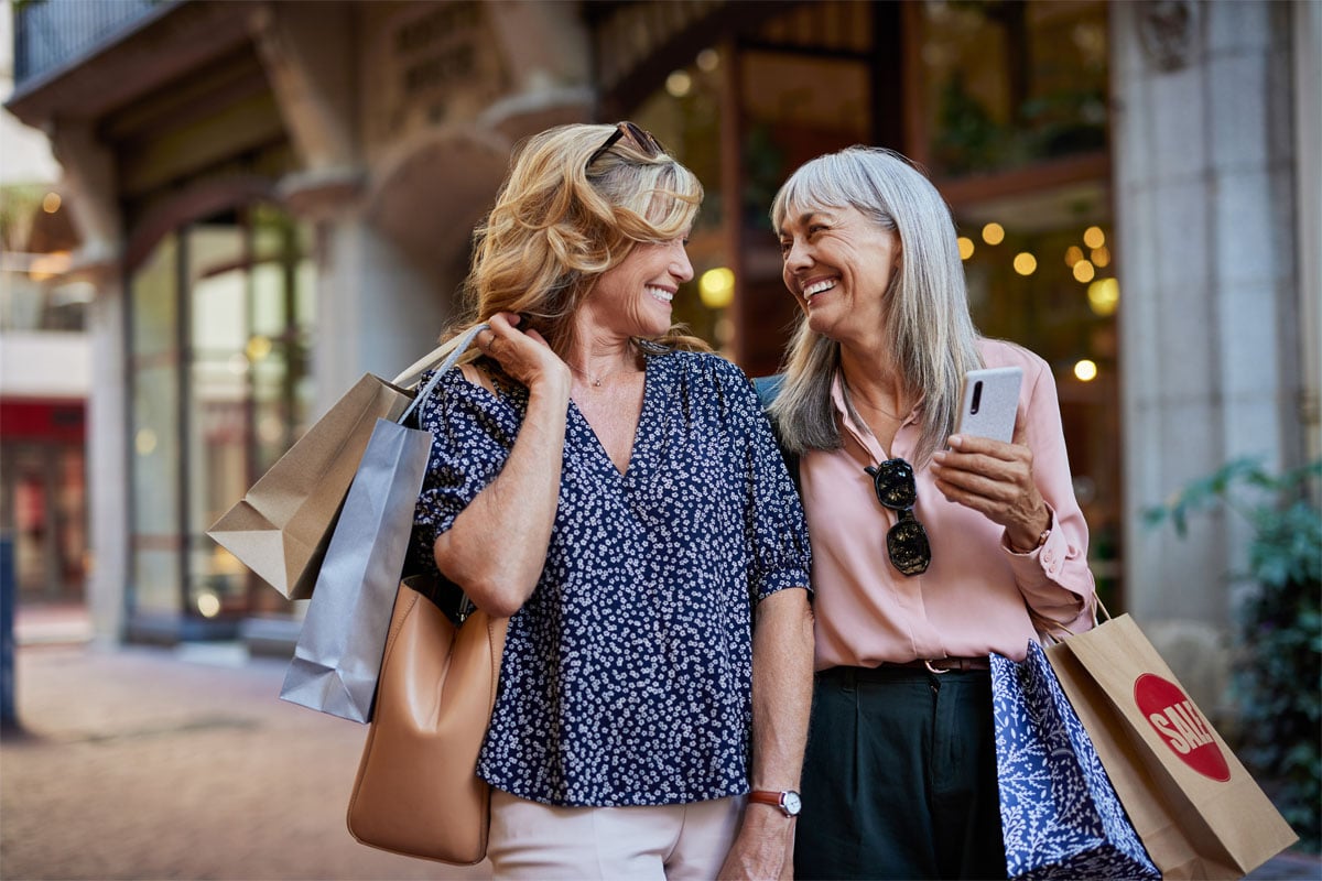 Happy mature women shopping together while looking at each other