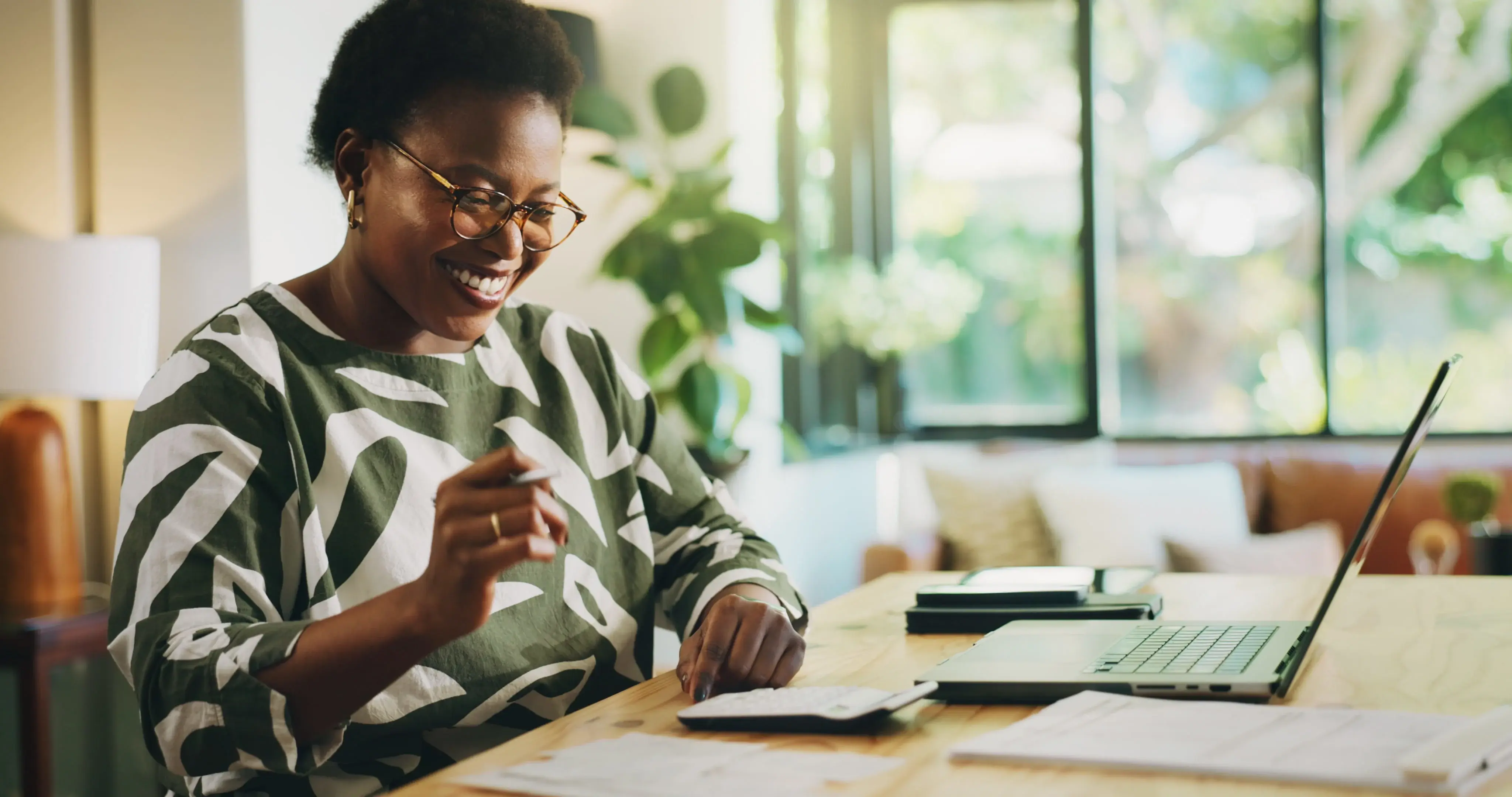 Happy, black woman and finance with laptop for payroll, tax return or budget planning at home.
