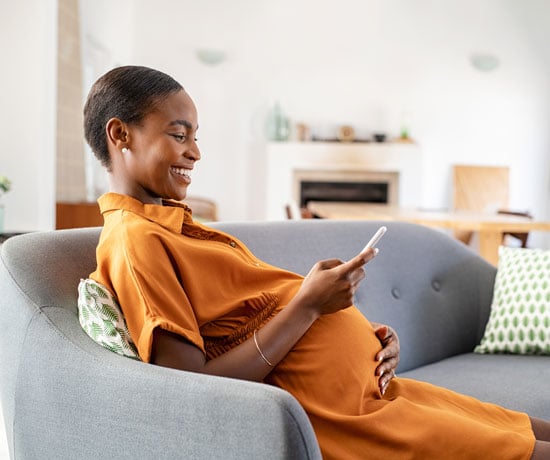 Pregnant black woman on couch with cellphone