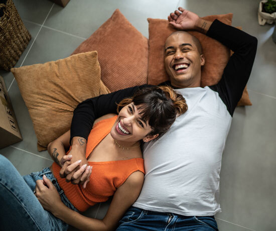 A smiling couple lying down on pillows on the floor